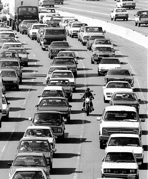 A highway with traffic at a stop and a motorcyclist driving between them.