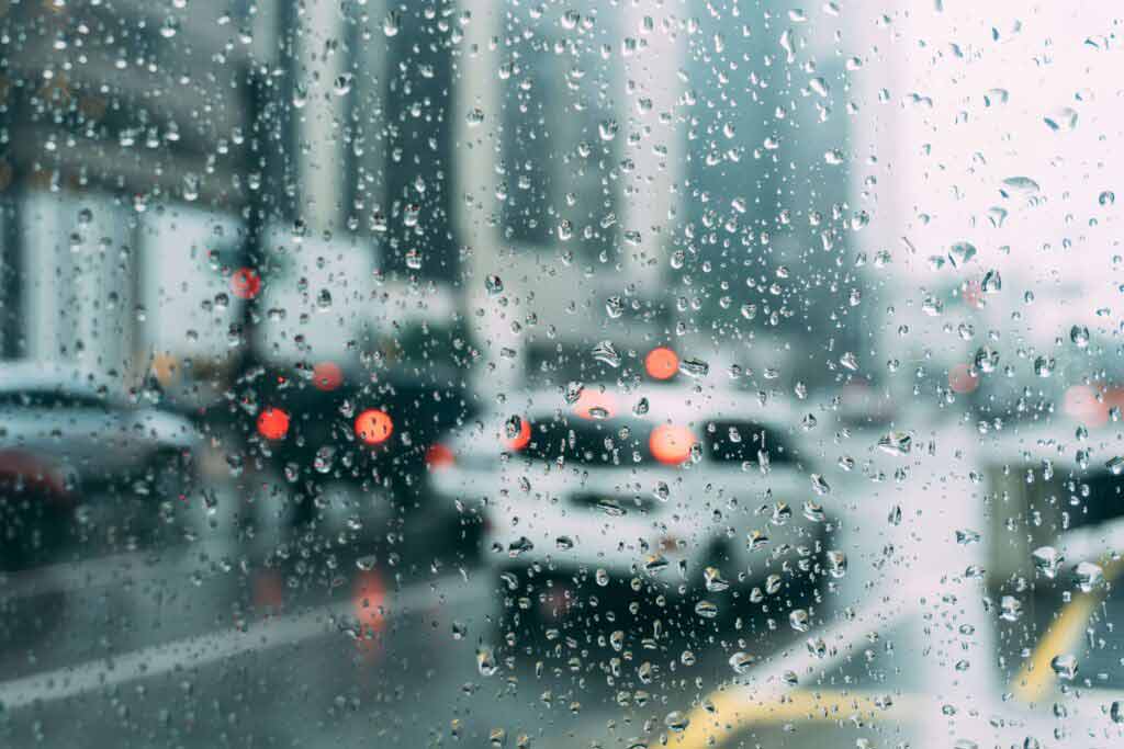 Cars drive in the rain, droplets cover the lens of the camera taking the picture.